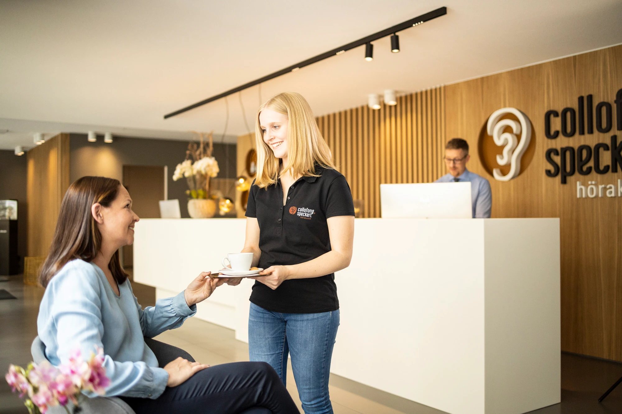 Mitarbeiterin bringt einer wartenden Kundin im Wartebereich einen Kaffee